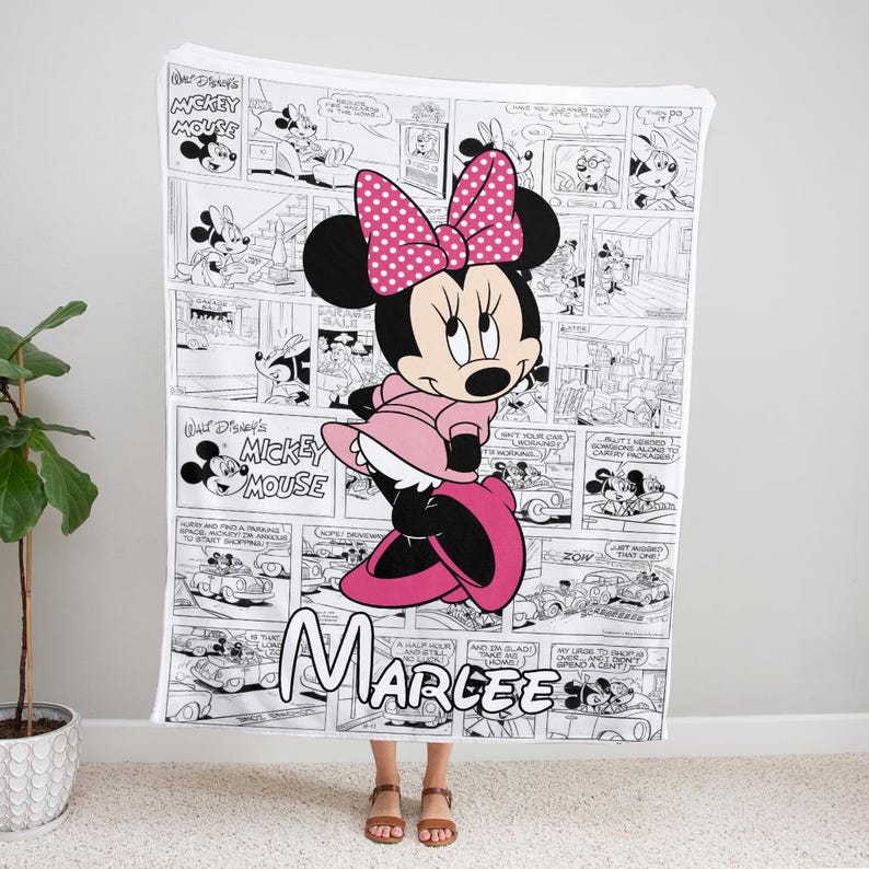 May include: A white blanket featuring a Minnie Mouse design. The blanket showcases a comic strip pattern with Minnie Mouse in a pink dress and bow. The name "Marlee" is written in cursive at the bottom.
