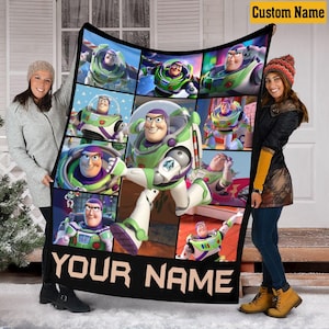 May include: A rectangular fleece blanket featuring a collage of Buzz Lightyear character images from the Toy Story franchise. The design includes a large central figure and smaller panels, with the text "YOUR NAME" printed in bold letters at the bottom.