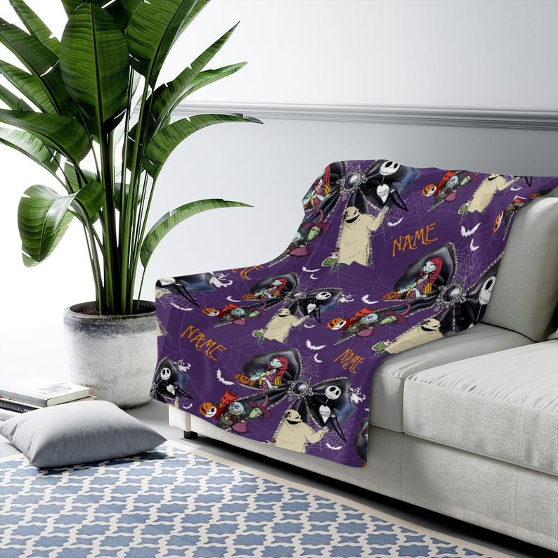May include: A purple fleece throw blanket featuring a repeating pattern of characters from The Nightmare Before Christmas, including Jack Skellington, Sally, and Oogie Boogie, interspersed with black bows, bats, and the customizable text NAME.