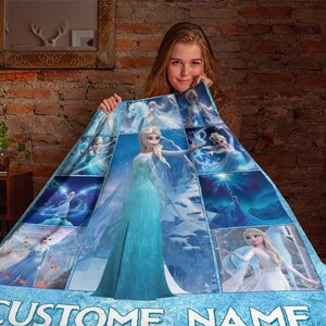 May include: A blue and white blanket featuring images of a princess in a blue dress. The blanket has a collage design with the words "CUSTOM NAME" at the bottom. The blanket is held up by a person.