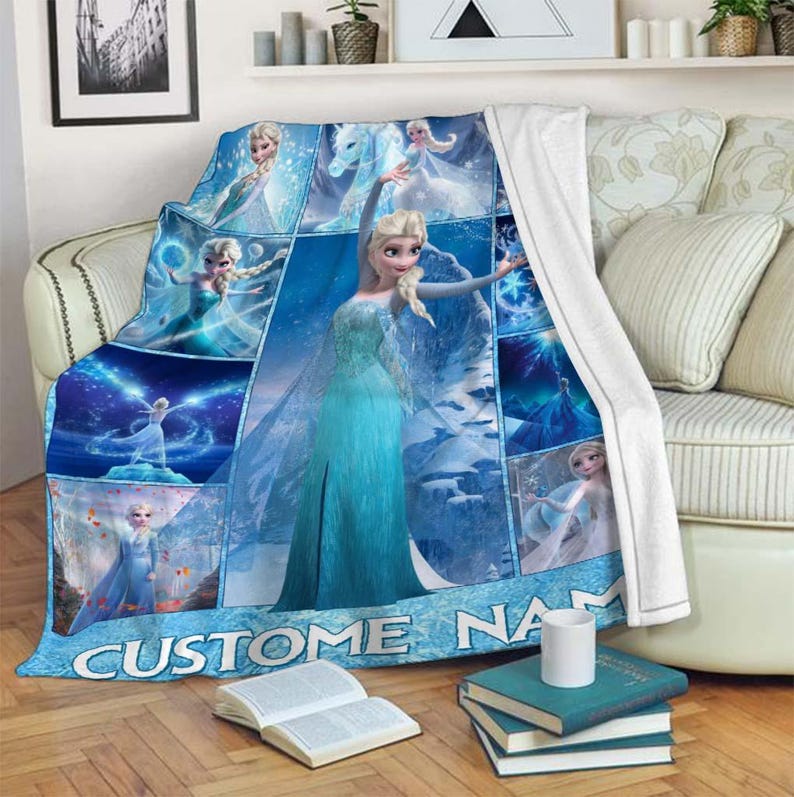 May include: A blue fleece blanket featuring multiple images of a character in a blue dress. The blanket has the text "CUSTOM NAME" in white letters at the bottom. The blanket is draped over a sofa.