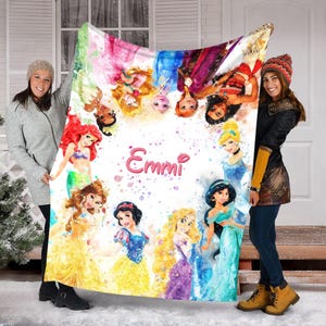 May include: A large, rectangular blanket featuring watercolor illustrations of various Disney princesses. The princesses are arranged in a circle around the name "Emmi" in pink script. The blanket has a white background with colorful paint splatters.