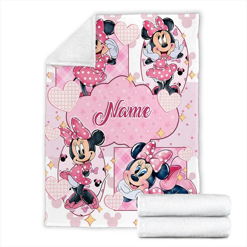 May include: A soft fleece blanket featuring a repeating pattern of Minnie Mouse in a pink polka dot dress and bow. The design includes pink hearts, stars, and a central cloud-shaped graphic with the word Name printed in a cursive script font.