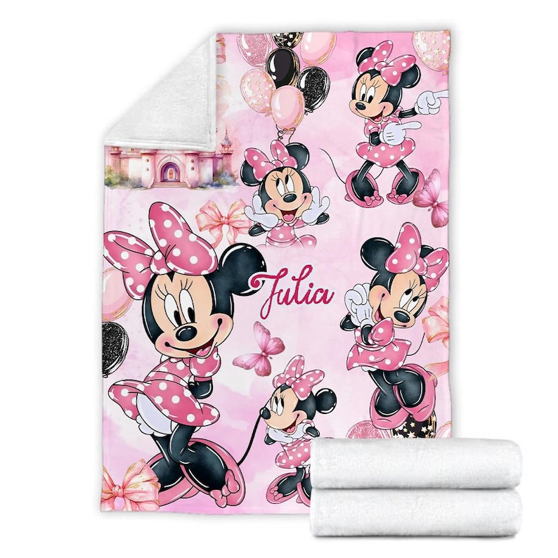May include: A soft fleece blanket featuring a repeating pattern of Minnie Mouse in a pink polka dot dress, pink bows, butterflies, and balloons against a light pink background. The name Julia is printed in a cursive script in the centre.