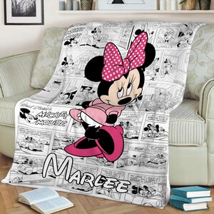 May include: A plush throw blanket featuring Minnie Mouse in a pink dress and bow, set against a black and white comic strip background. The blanket has the name "Marlee" printed on it, and the words "Walt Disney's Mickey Mouse" are also visible.