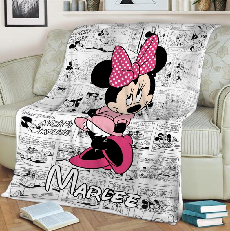 May include: A plush throw blanket featuring Minnie Mouse in a pink dress and bow, set against a black and white comic strip background. The blanket has the name "Marlee" printed on it, and the words "Walt Disney's Mickey Mouse" are also visible.