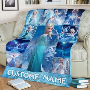 May include: A blue fleece blanket featuring multiple images of a princess in a blue dress. The blanket has the text "CUSTOM NAME" in white letters on a light blue background. The blanket is draped over a beige sofa.