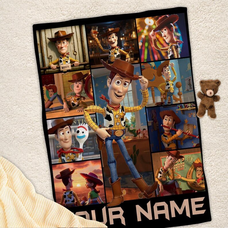 Op de afbeelding: Een zwarte deken met een collage van afbeeldingen van het personage Woody uit de animatiefilm Toy Story. De deken heeft een grote afbeelding van Woody in het midden, met kleinere afbeeldingen eromheen. Rechts staat een kleine bruine teddybeer.