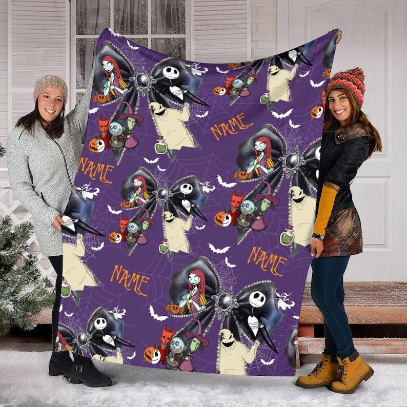 May include: A purple fleece blanket featuring a repeating pattern of black bows, white spiderwebs, and characters from The Nightmare Before Christmas, including Jack Skellington, Sally, and Oogie Boogie, with the orange text "NAME" printed on it.