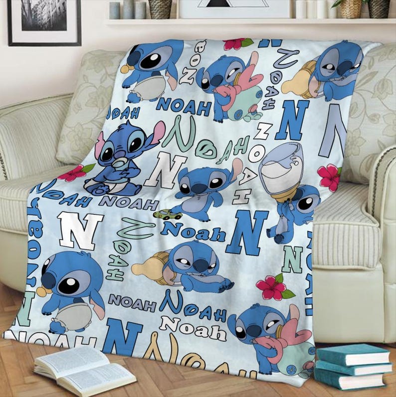 Może przedstawiać: Jasnoniebieski koc z postacią z kresk&oacute;wki Stitch w r&oacute;żnych pozach. Na kocu nadrukowano imię "Noah" i literę "N". Czerwone kwiaty i butelka dla dziecka są r&oacute;wnież widoczne.