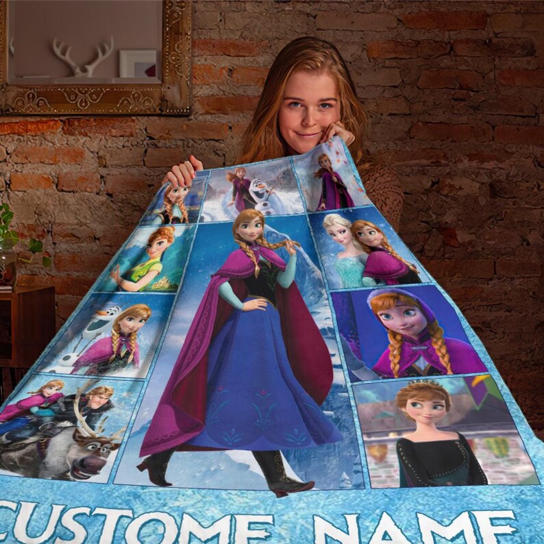 May include: A blue and purple blanket featuring images of characters from the animated movie Frozen. The blanket has a central image of Anna, surrounded by other characters. The words "CUSTOM NAME" are at the bottom.