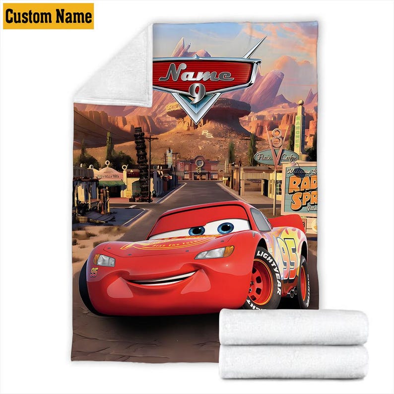 May include: A plush, white blanket featuring a vibrant illustration of Lightning McQueen from the movie Cars. The design includes the character, the Radiator Springs sign, and the text "Name 9". The blanket has a custom name option.