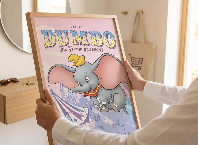 May include: A framed poster featuring the Disney character Dumbo, a gray elephant with large pink ears and a yellow hat. The text reads Disney Dumbo The Flying Elephant. The background shows a circus scene with a Ferris wheel in soft purple tones.