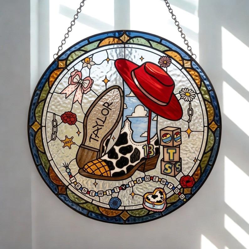 May include: A circular stained glass suncatcher featuring a cow-print cowboy boot with the name TAYLOR on the sole and the number 13 on the side. A red hat, alphabet blocks spelling TSS, a pink bow, and a beaded string with text I KNEW YOU.