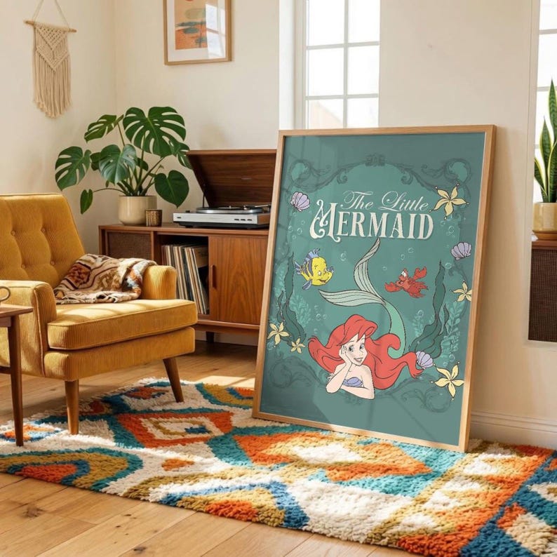 May include: A rectangular wall art print featuring The Little Mermaid with Ariel, Flounder, and Sebastian in a teal frame. The design includes red hair, yellow and blue fish, a red crab, and white flowers on a muted teal background with text.