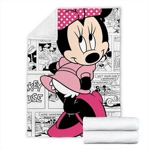 May include: A pink Minnie Mouse blanket featuring a comic strip design in black and white. Minnie Mouse is depicted in a pink dress and bow. Two folded white blankets are at the bottom. The comic strip includes the text "SALE", "KEY USE", and speech bubbles.