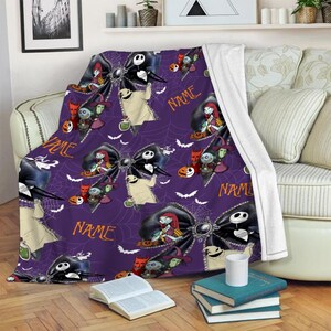 May include: A purple fleece throw blanket featuring a repeating pattern of black bows, white spiderwebs, and characters from The Nightmare Before Christmas, including Jack Skellington and Sally. The word NAME is printed in orange text.