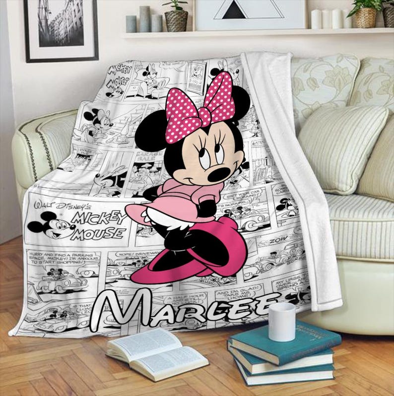 May include: A white blanket featuring a Minnie Mouse design. The blanket has a black and white comic strip pattern with a large image of Minnie Mouse in pink. The name "Marlee" is printed on the blanket.