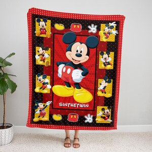 May include: A red and black Mickey Mouse blanket featuring multiple images of Mickey Mouse. The blanket has a red border with white polka dots. The center of the blanket has a large image of Mickey Mouse with the text "SINTHETWIN".