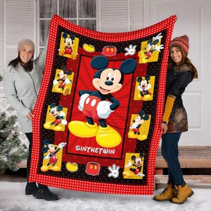 May include: A red and black Mickey Mouse blanket. The blanket features a large image of Mickey Mouse in the center, surrounded by smaller images of Mickey. The border is red with white polka dots. The text "SINTHET@IN" is visible.
