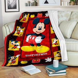 May include: A red and black Mickey Mouse throw blanket. The blanket features a large image of Mickey Mouse in the center, surrounded by smaller images of Mickey. The text "SINTHETWIN" is printed on the blanket.