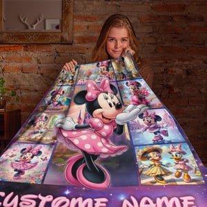 May include: A colorful blanket featuring Minnie Mouse in various poses. The blanket has a pink and purple color scheme, with a large central image of Minnie Mouse in a pink polka-dot dress. The blanket is made of soft material.