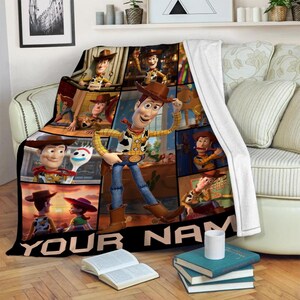 Op de afbeelding: Een zachte deken met een collage van afbeeldingen van het personage Woody uit de animatiefilm Toy Story. De deken heeft een zwarte rand met de tekst "YOUR NAME" in het wit. De hoofdafbeelding toont Woody in zijn cowboy-outfit.