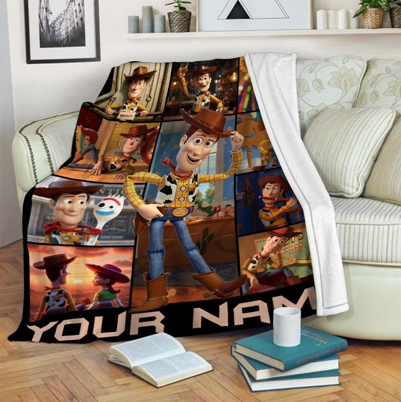 Op de afbeelding: Een zachte deken met een collage van afbeeldingen van het personage Woody uit de animatiefilm Toy Story. De deken heeft een zwarte rand met de tekst "YOUR NAME" in het wit. De hoofdafbeelding toont Woody in zijn cowboy-outfit.