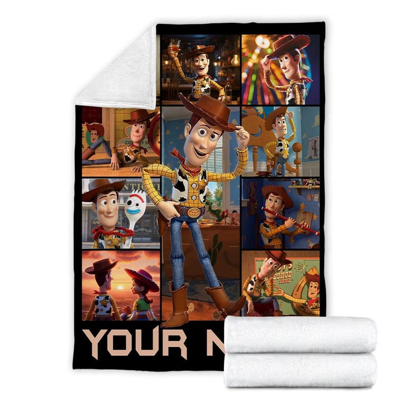 Op de afbeelding: Een zwart-witte deken met een collage van afbeeldingen van het personage Woody uit de animatiefilm Toy Story. De deken heeft een witte, zachte onderkant en een zwarte rand met de tekst "YOUR N".