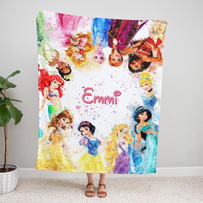 May include: A colorful blanket featuring watercolor illustrations of various princesses. The blanket has a pink name in the center, surrounded by the princesses in their iconic outfits. The blanket is made of soft material.