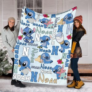 Może przedstawiać: Jasnoniebieski koc z postacią Stitcha z Lilo & Stitch. Koc ma wiele obraz&oacute;w Stitcha, imię "Noah" i literę "N" w zabawnej czcionce. Czerwone kwiaty są r&oacute;wnież rozrzucone po kocu.