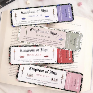 Può includere: Quattro segnalibri decorativi con il testo "Kingdom of Ilya Book Club" e citazioni di Lauren Roberts. Ogni segnalibro presenta un design diverso con corone, spade e dettagli floreali. I segnalibri sono sopra un libro aperto.