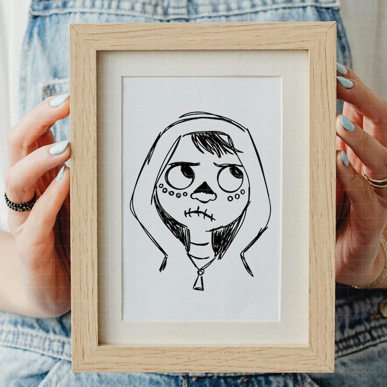 Puede incluir: Un boceto en blanco y negro enmarcado de un personaje con rostro de calavera, que lleva una sudadera con capucha. La obra de arte est&aacute; en un marco de madera de color claro. El personaje tiene ojos grandes y una boca cosida.