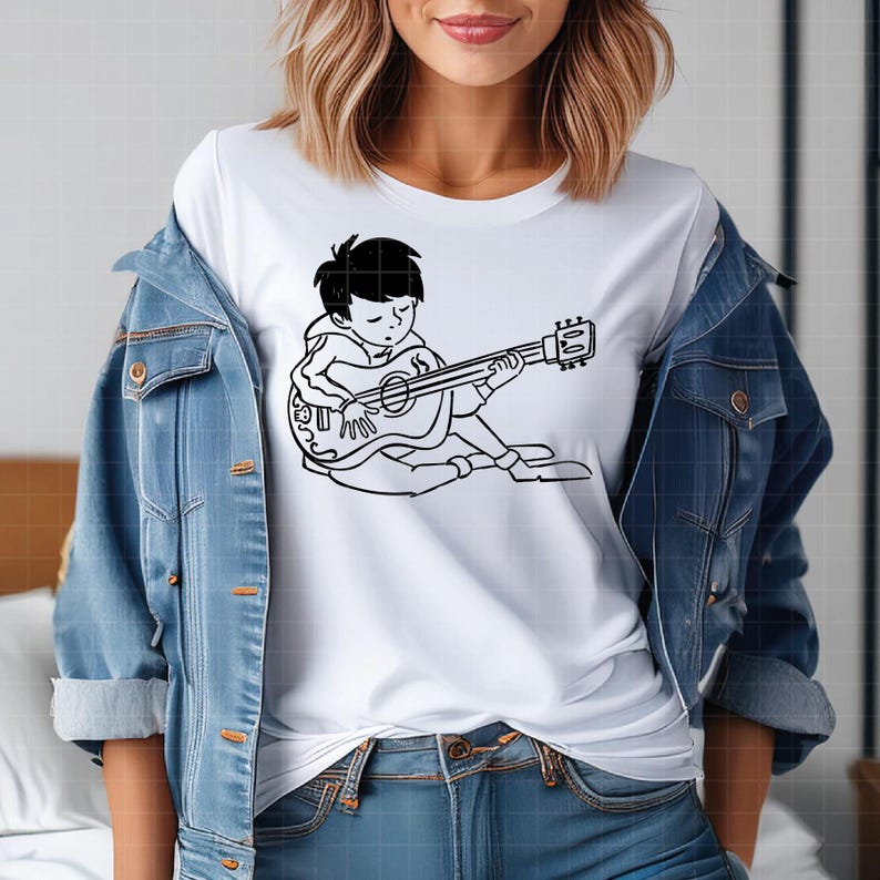Puede incluir: Camiseta blanca con una ilustraci&oacute;n en blanco y negro de una persona tocando una guitarra ac&uacute;stica. El gr&aacute;fico muestra una figura sentada con los ojos cerrados, sosteniendo la guitarra. La camiseta se usa con una chaqueta vaquera azul.