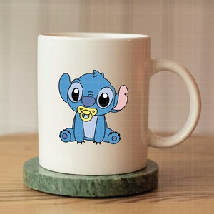 Pu&ograve; includere: Tazza in ceramica bianca con un personaggio dei cartoni animati blu, con grandi occhi neri, un ciuccio e grandi orecchie. Il personaggio &egrave; sulla tazza. La tazza &egrave; su un sottobicchiere verde.