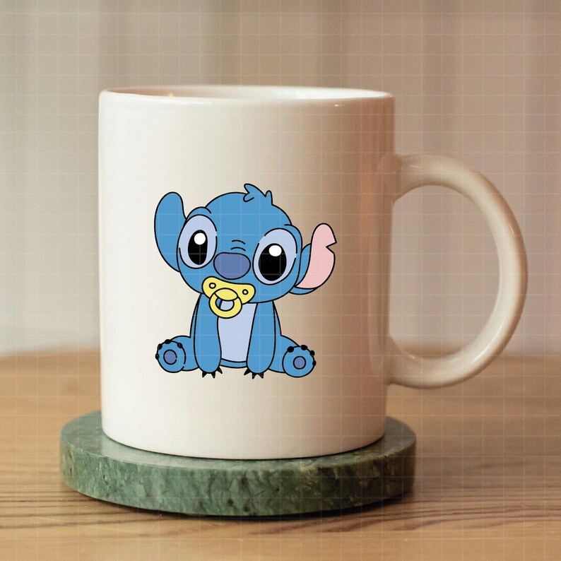 Pu&ograve; includere: Tazza in ceramica bianca con un personaggio dei cartoni animati blu, con grandi occhi neri, un ciuccio e grandi orecchie. Il personaggio &egrave; sulla tazza. La tazza &egrave; su un sottobicchiere verde.