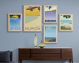 May include: Five framed prints of vintage travel posters for the Great Lakes. The posters feature illustrations of the lakes and the names "Lake Ontario", "Lake Huron", "Lake Erie", "Lake Michigan", and "Lake Superior". The prints are displayed on a light blue wall above a dark brown wooden dresser.