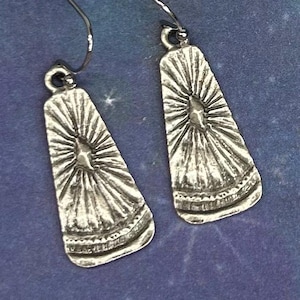 May include: A pair of silver-toned earrings. Each earring has a trapezoid shape with a sunburst design. The earrings hang from a simple hook. The earrings are displayed on a blue background with a starry pattern.