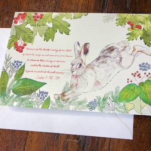 May include: A watercolor illustration of a white rabbit leaping through a forest scene. The background features green leaves, red berries, and blue flowers. The image includes a bible verse: "Because of the tender mercy of our God, by which the rising sun will come to us from heaven to shine on those living in darkness and on the shadows of death, to guide our feet into the path of peace. Luke 1:78-79."