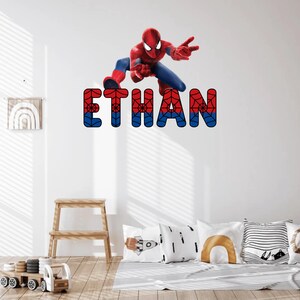 May include: A wall decal featuring Spider-Man in a dynamic pose above the name "ETHAN" in red and blue web-patterned letters. The room includes a wooden step stool, decorative pillows, and a wooden toy truck.