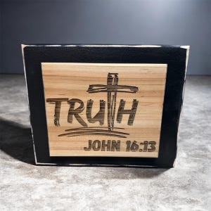 May include: Wooden plaque with the word "TRUTH" and a cross engraved on a light brown surface. The text "JOHN 16:13" is below. The plaque is framed with a black border.