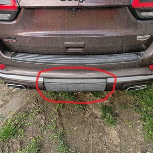 Könnte beinhalten: Rückansicht eines braunen Jeep Grand Cherokee. Das Bild konzentriert sich auf den unteren Stoßfängerbereich mit einer dunkelgrauen Trittstufe und einer schwarzen Zierleiste. Das Jeep-Logo ist oben sichtbar.