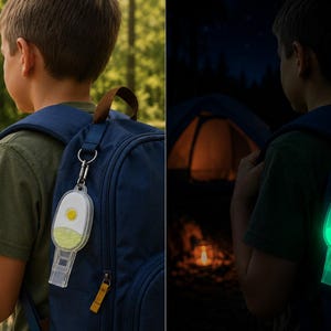 Puede incluir: Un llavero transparente con forma de silbato, sujeto a una mochila azul. El llavero tiene una carcasa blanca con un botón amarillo y un interior verde que brilla en la oscuridad. La imagen muestra el llavero a la luz del día y brillando por la noche.
