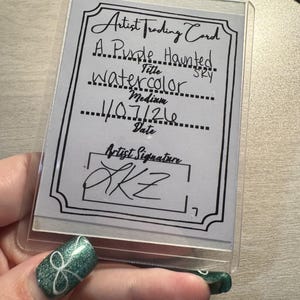 May include: An artist trading card in a clear plastic sleeve. The card features the title "A Purple Haunted Sky" and the medium "Watercolor." The date is 1/07/21, and the artist's signature is "AKZ."