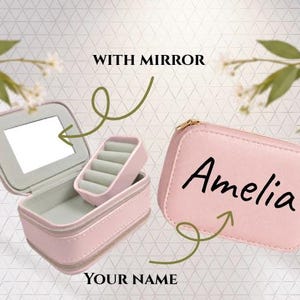 Puede incluir: Un joyero rectangular de color rosa claro con cierre de cremallera. El interior cuenta con un espejo integrado y una bandeja extraíble para anillos de terciopelo gris. El exterior del estuche cerrado está personalizado con el texto Amelia en negro.
