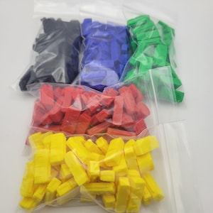 Peut inclure: Cinq sacs en plastique transparents remplis de pièces de jeu rectangulaires colorées. Les pièces sont de couleurs noir, bleu, vert, rouge et jaune. Les sacs sont disposés en léger chevauchement sur fond blanc.