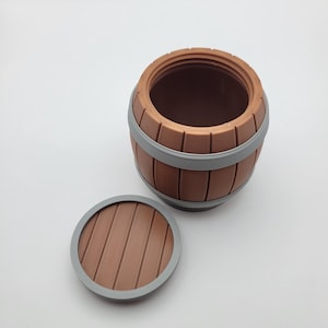 May include: A brown barrel-shaped container with a removable lid. The barrel has gray bands and a matching lid with a gray rim. The container is made of a wood-like material and is designed to resemble a miniature barrel.