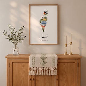 May include: A framed art print depicting the map of Palestine, adorned with vibrant floral and geometric designs. The print includes Arabic script and the English word "Palestine". The artwork hangs above a wooden cabinet, complemented by a decorative table runner.