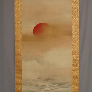 以下が含まれることがあります： 水面に沈む赤い太陽を描いた日本の掛け軸。作品は、花柄の金色の縁と下部の木製のローラーが特徴です。 全体的な色使いは、ベージュ、オレンジ、グレーの色合いで表現されています。