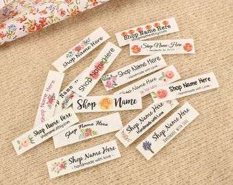 May include: A collection of ten white rectangular hang tags with floral designs and the text "Shop Name Here" printed on them. Some tags include the text "Handmade with Love" and a website address.